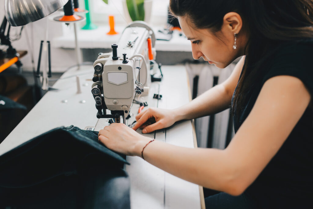 female artisan threading black leather on sewing machine, close